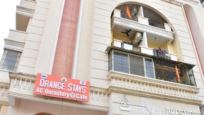 A multi-story building with a sign for Orange Stays AC Dormitory & Cafe, Equitas Small Finance Bank, and Rudra Prestige.
