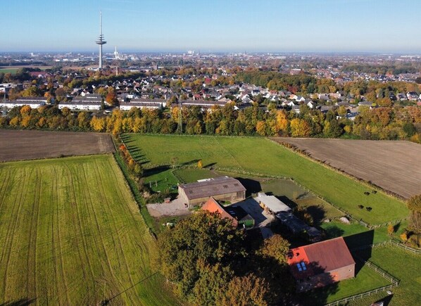 An aerial view of a rural area with fields, a farmhouse, and a distant tower.