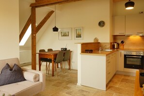 A cozy kitchen with a dining area, wooden beams, a built-in oven, and a small island with a sink.