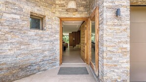 A stone-walled hallway leading to a modern interior with a wooden door and a window.