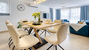 A modern living room with a blue sofa, a dining area with a table set for four, and a large wall clock. - Villa Mare With Private Pool And Garden (Malinska-Dubasnica)