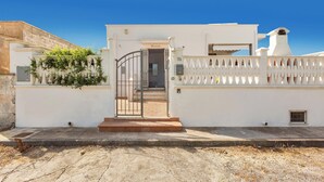 Un bâtiment blanc avec une entrée fermée par un portail, une petite fenêtre et une cheminée.