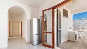 Une cuisine moderne équipée d’un réfrigérateur, d’une porte coulissante à cadre en bois et offrant une vue sur la mer grâce à une fenêtre à motifs.