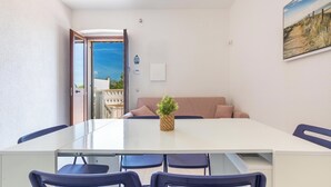 Un coin repas avec une table blanche, des chaises bleues, un canapé beige et une petite plante en pot.