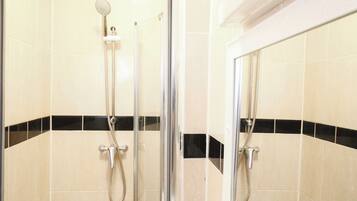 A glass-enclosed shower area with a handheld showerhead and a wall-mounted faucet.