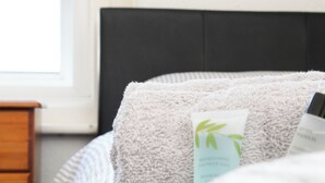 A bed with a fluffy pillow and a bottle of lotion. - Pebbles Guest house (Southampton)