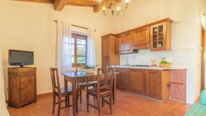 A kitchen with wooden cabinets, a dining table with chairs, and a television on a cabinet.