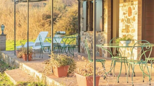 An outdoor patio with a stone wall, green metal chairs, and potted plants.