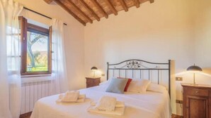 A bedroom with a bed, two bedside tables, a window with curtains, and a view of greenery outside.