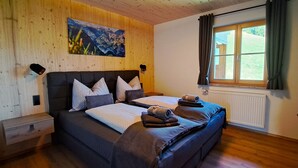 A bedroom with a wooden headboard, a large bed with multiple pillows, a window with curtains, and a painting on the wall. - Apartment "wegmo-1" in Ruhiger Höhenlage in Bischofshofen im Salzburger Land (Bischofshofen)