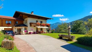 A two-story wooden house with a balcony, surrounded by greenery and mountains. - Apartment "wegmo-1" in Ruhiger Höhenlage in Bischofshofen im Salzburger Land (Bischofshofen)
