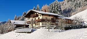 A chalet-style building with a balcony, surrounded by snow-covered trees and a clear blue sky.