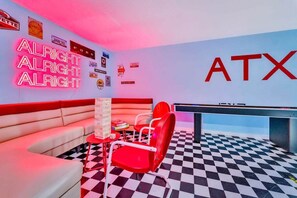 A room with a neon sign reading 'ALRIGHT ALRIGHT ALRIGHT,' a checkered floor, a red and white sofa, and a red chair.