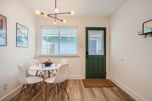 A dining area with a table and chairs, a green door, and a window with blinds.