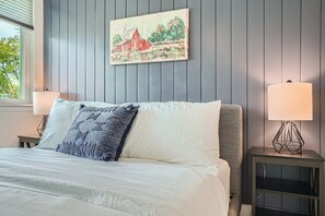 A bedroom with a bed, two bedside lamps, a nightstand, and a wall-mounted painting.