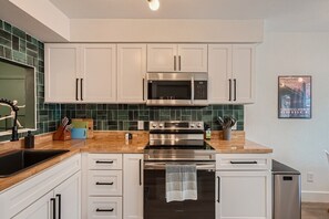 A modern kitchen with white cabinets, a stainless steel microwave, an oven, and a dishwasher.