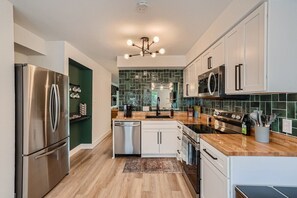 A modern kitchen with stainless steel appliances, white cabinetry, and a green backsplash.