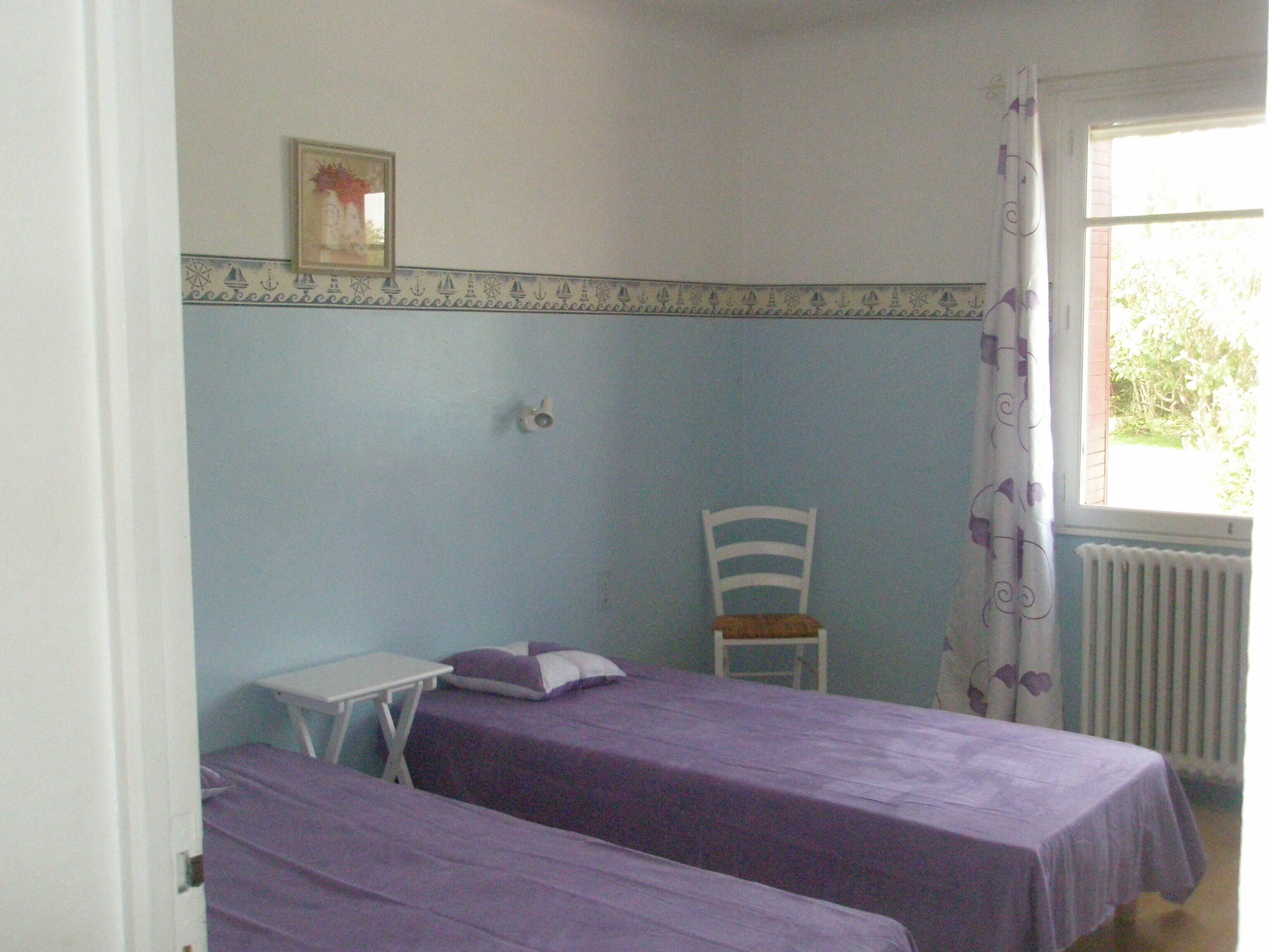 A room with two beds, a small table, a chair, and a window with curtains.