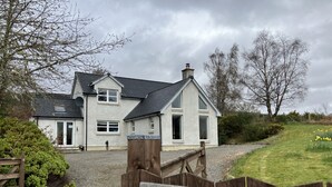 A two-story house with a gravel driveway and a wooden gate labeled "OISEVAL." - Oiseval is a pet friendly cottage with magnificent views. (Fort Augustus)