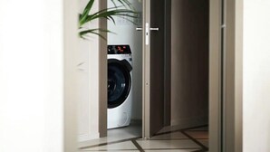 A view of a washing machine in a hallway with a tiled floor and a door leading to another room. - Sustainably Operated One-Bedroom Apartment in Central London (London)