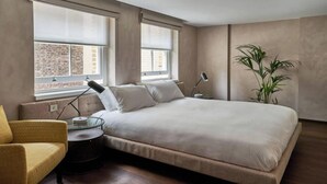 A modern bedroom with a large bed, a small side table, a chair, and a potted plant. - Sustainably Operated One-Bedroom Apartment in Central London (London)