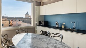 Een moderne keuken met een marmeren tafel en stoelen, een blauwe accentmuur en uitzicht op een historisch gebouw door een raam.