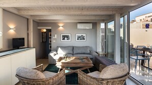 Een moderne woonkamer met een houten plafond, een bank, een salontafel, rieten stoelen en een televisie.