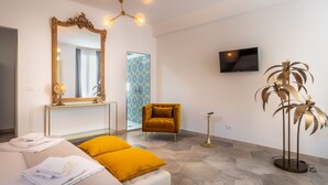 Habitación de hotel con cama, un espejo grande, televisión, una mesita pequeña y una lámpara de pie decorativa.