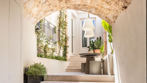 Una escalera conduce a un balcón con una lámpara colgante, rodeado de plantas y un arco de piedra rústica.