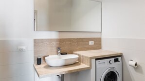 A modern bathroom with a white sink, a beige countertop, a mirror, and a washing machine.