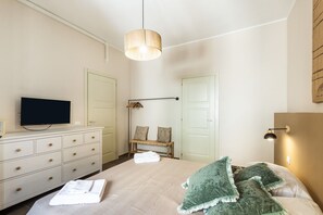 A bedroom with a bed, a dresser, a television, a hanging light, and a door.