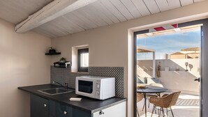 Een kleine keuken met een magnetron, donkere kastjes en een klein raam.