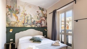Een hotelkamer met een bed, een schilderij aan de muur, een raam met gordijnen en uitzicht op gebouwen.