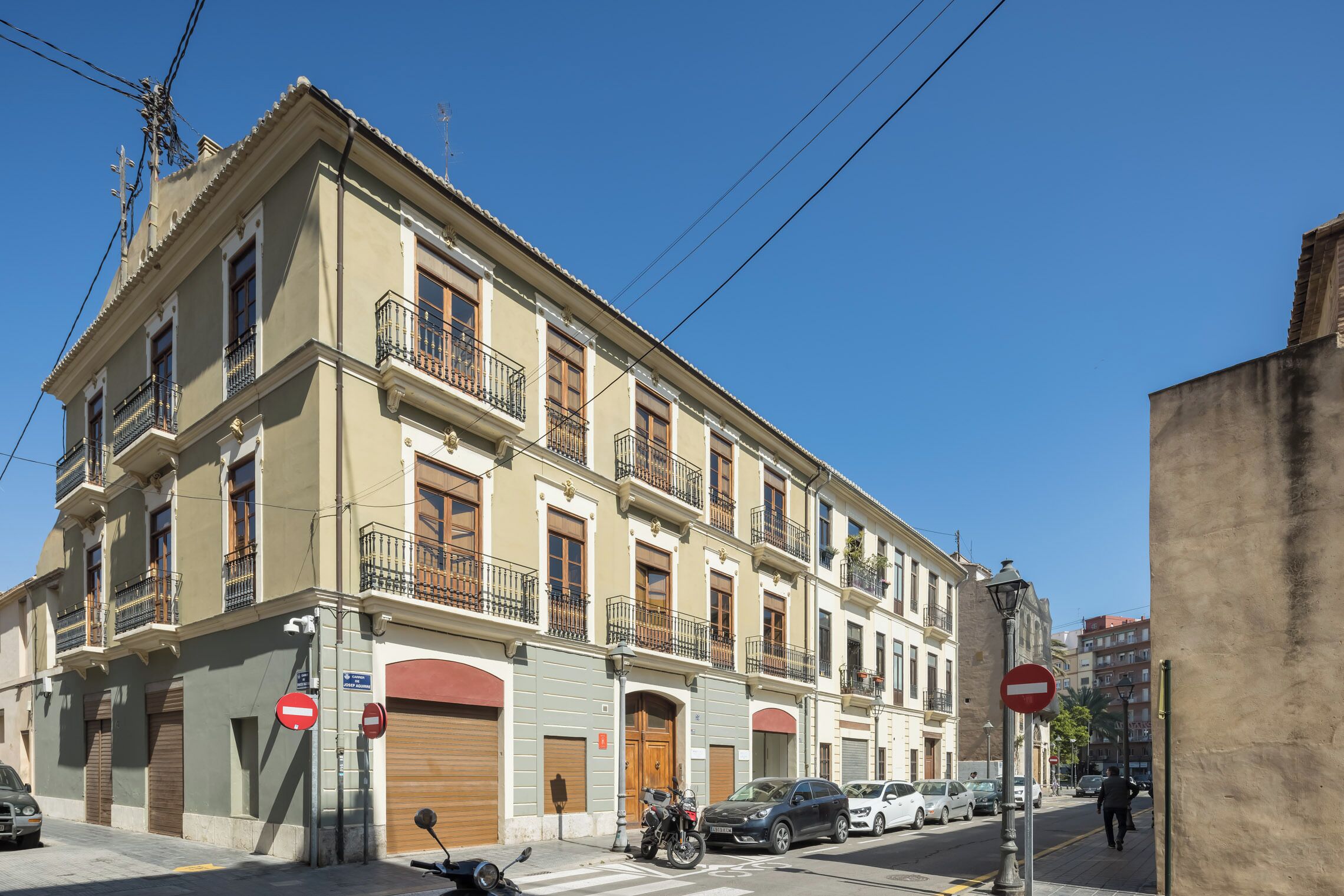 Un edificio de varios pisos con balcones, una motocicleta estacionada al frente y un cielo azul despejado.