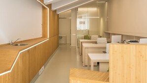 A modern kitchen with wooden cabinetry, a stainless steel sink, and a long countertop. There are white chairs and a table in the background. - Macflats Valencia Puerto (Valencia)