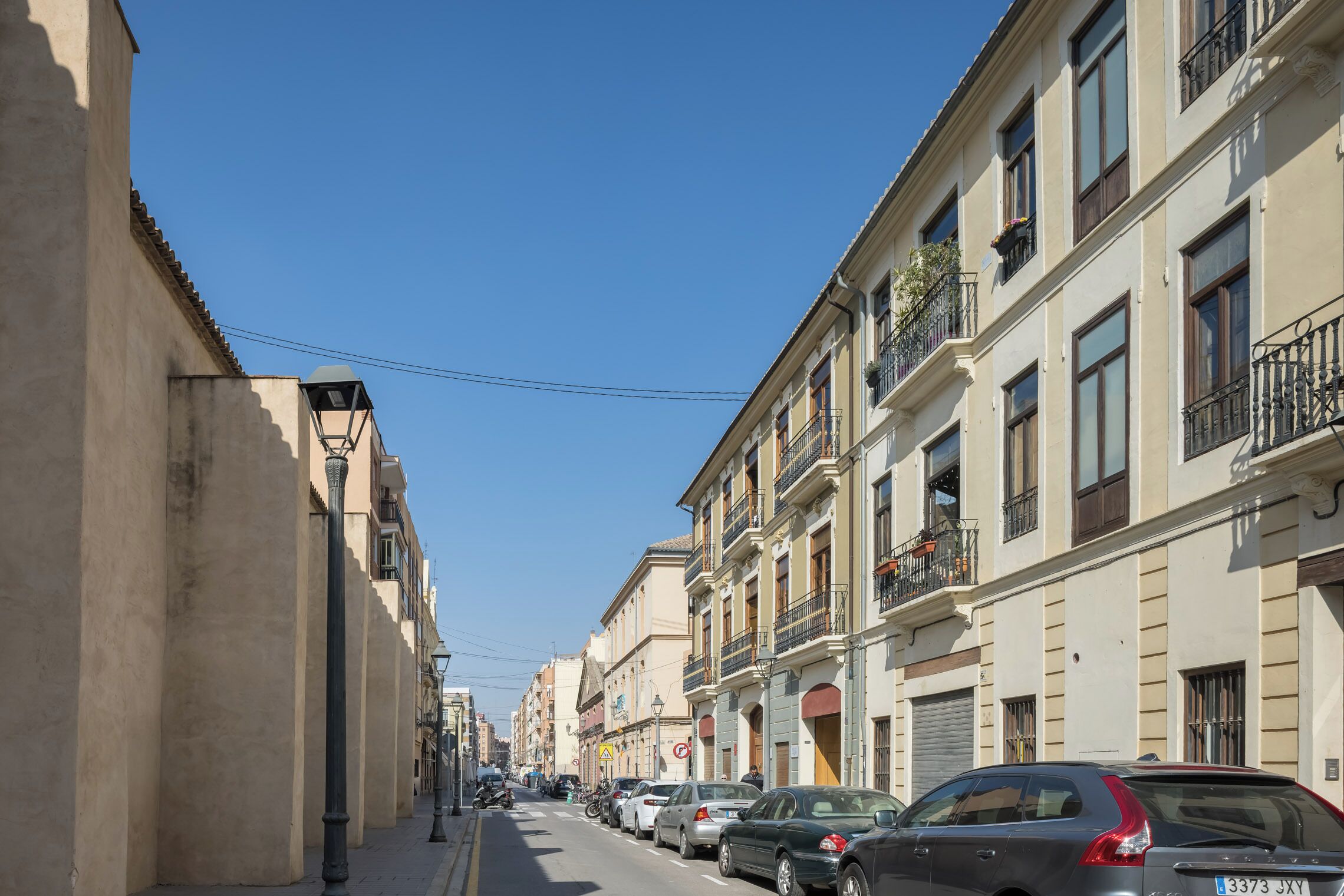 Una calle bordeada de coches aparcados y edificios con balcones.