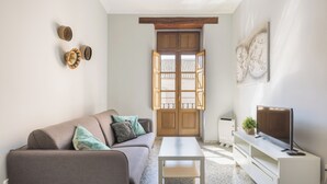 A living room with a sofa, coffee table, TV, and a window with open shutters. - Macflats Valencia Puerto (Valencia)