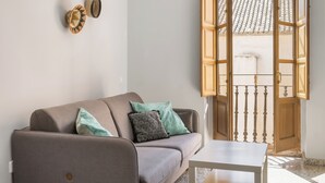 A living room with a sofa, a small table, and a wooden door with an open view to the outside. - Macflats Valencia Puerto (Valencia)