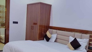 A bedroom with a large bed, a wardrobe, and a nightstand. - Madhav Residency (Mathura)