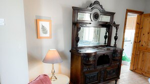 A room with a wooden cabinet, a small round table with a lamp, a chair, and a framed leaf artwork on the wall. - Lisheenbawn Farmhouse Farranfore (Castleisland)