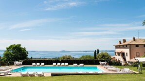 Una piscina con sillones de descanso, vista al mar y un edificio con techo de tejas.