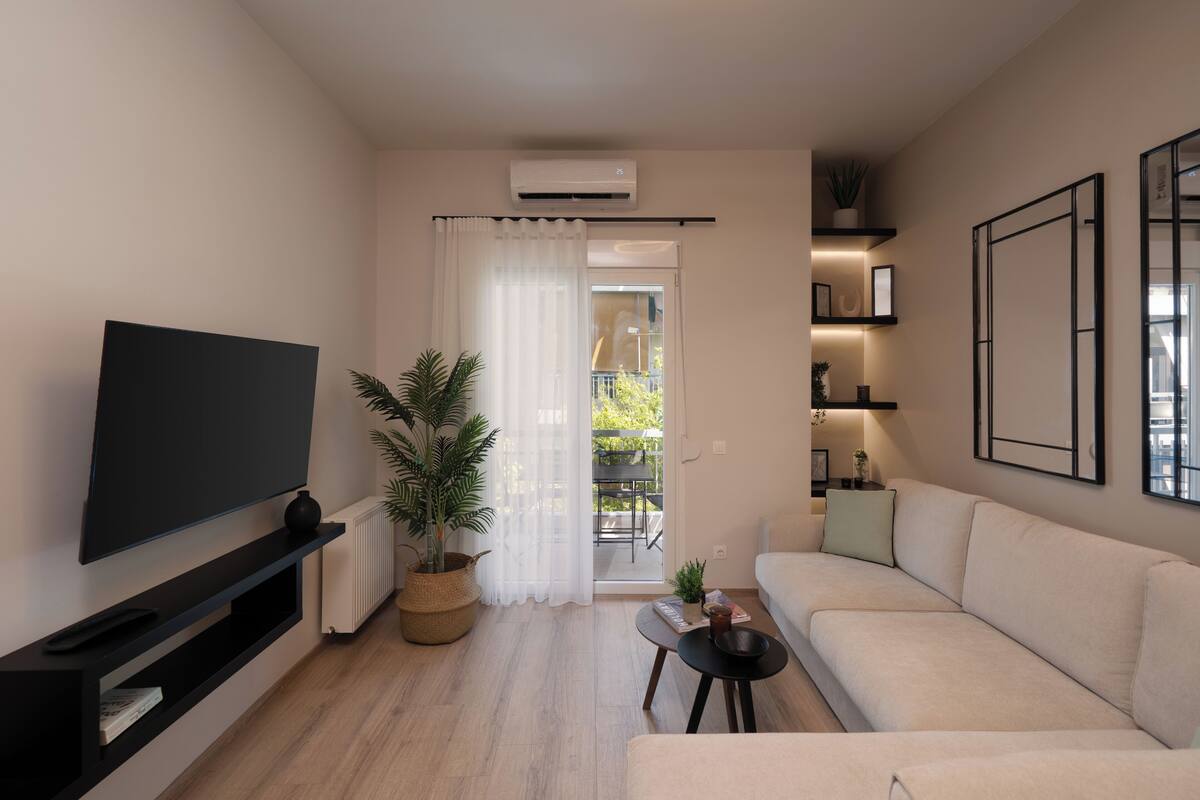 Una sala de estar moderna con un televisor de pantalla plana, un sofá, una pequeña mesa de centro y una planta en maceta.