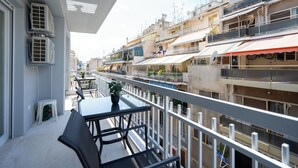 Un balcon avec une table et des chaises, donnant sur une zone urbaine densément construite, avec de nombreux immeubles.