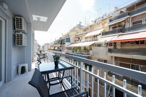 Varanda com mesa e cadeiras, dando vista para uma área urbana densamente povoada com vários edifícios.