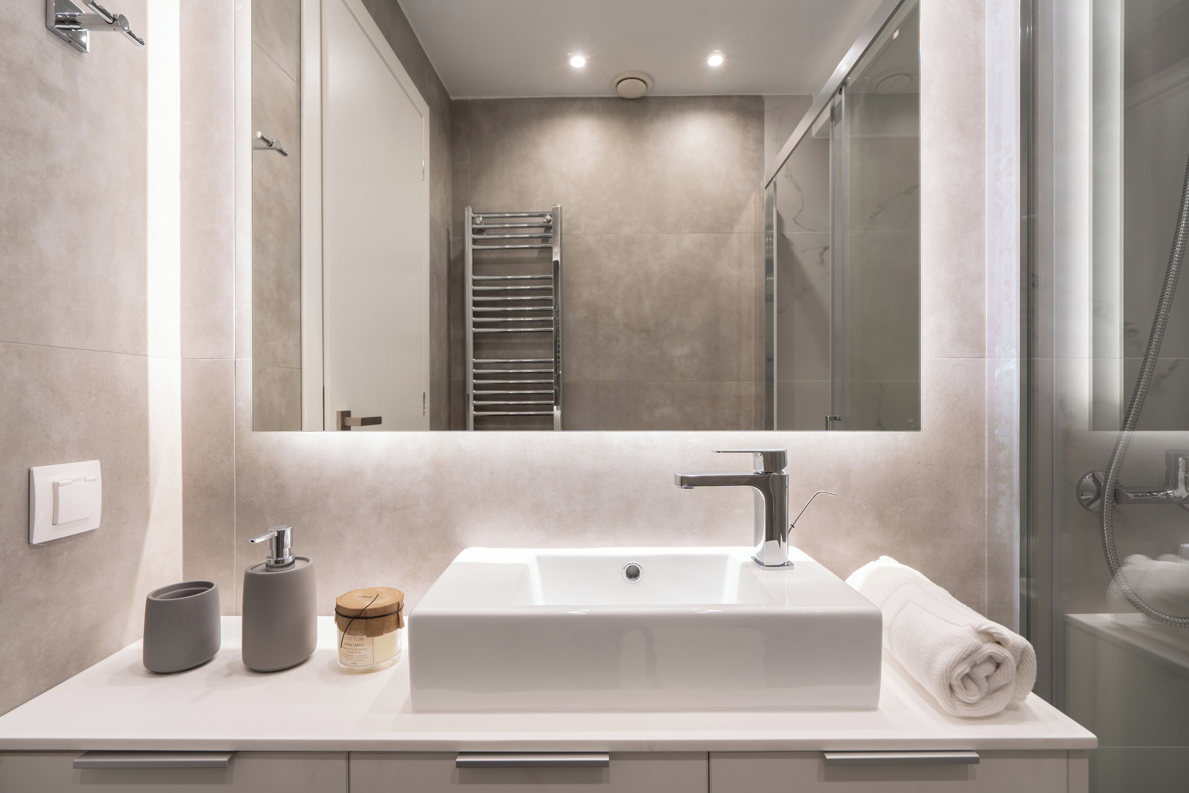 A modern bathroom with a large mirror, a rectangular sink, a towel, and a glass shower enclosure.