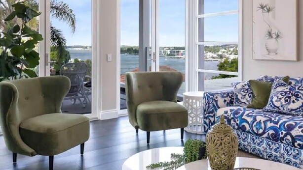 A living room with a sofa, two armchairs, a coffee table, and a view of a body of water through large glass doors. - Brisbane Hamilton Hill With Panorama View (Hamilton)