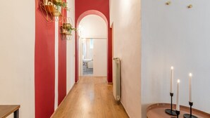 A hallway with a wooden floor, red walls, and a white door at the end. There are two black candle holders on a round table. - Wine Apartments Florence Prosecco (Firenze)