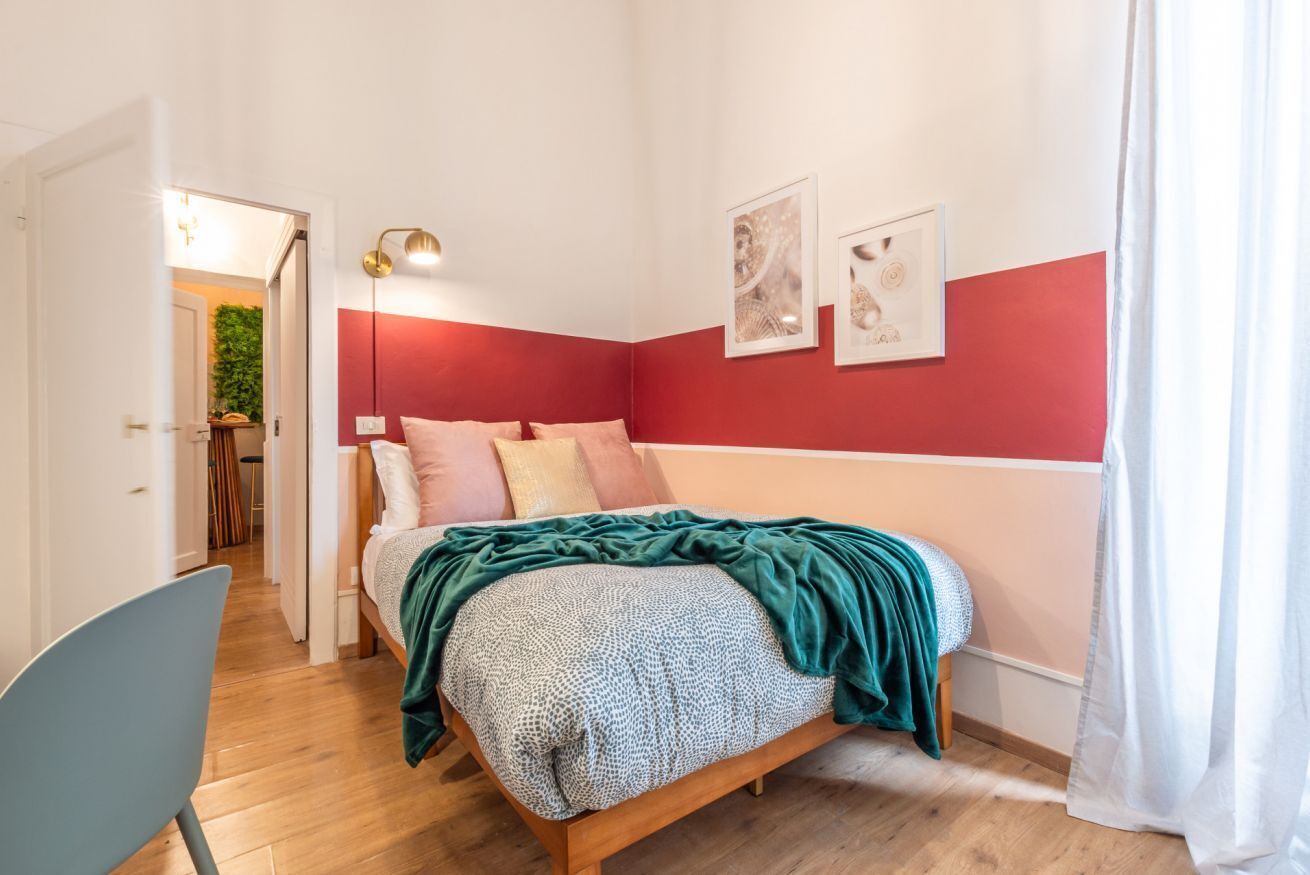 A bedroom with a bed, a chair, a lamp, and two framed pictures on the wall.