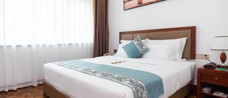A neatly made bed with a patterned throw, a bedside table with a lamp, and a painting on the wall.