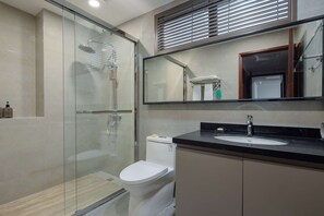 A modern bathroom with a glass shower enclosure, a white toilet, a sink with a black countertop, and a large mirror above the sink.